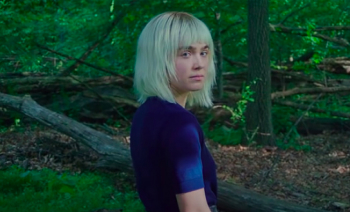 Ada portant un top bleu. Elle se trouve dans une fôret et se retourne pour nous faire