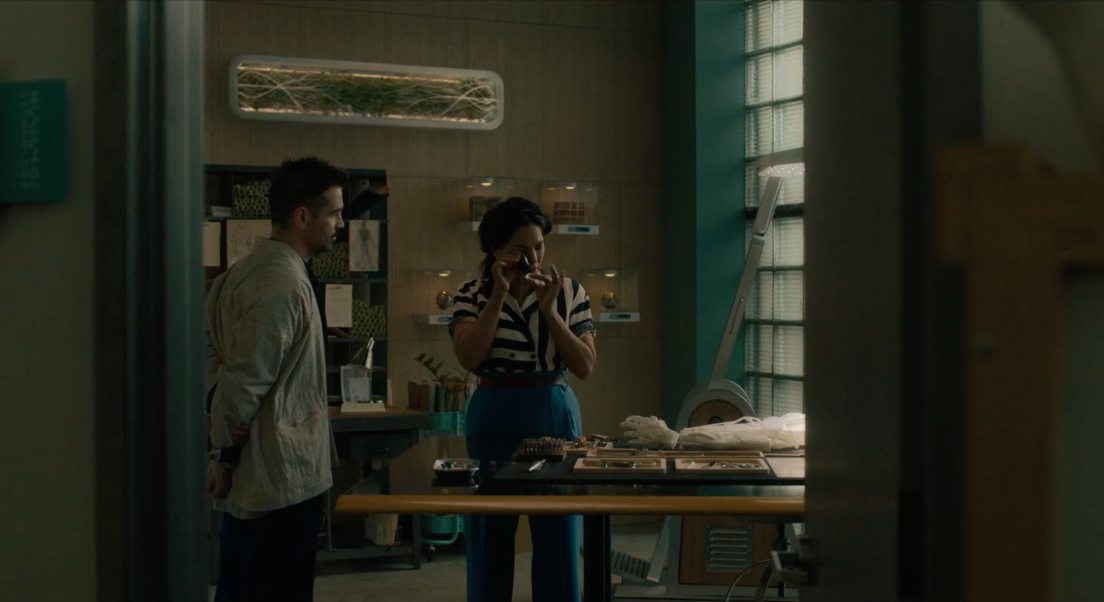 Cleo examine la pièce du système central de Yang. Jake est à côté et la regarde faire. Sur la table devant eux se trouvent différents objets scientifiques.