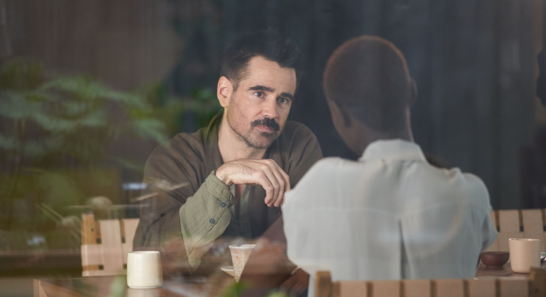 Jake et Kyra discutent à un table. Des boissons et plats sont situés devant eux. Kyra est de dos, Jake nous fait face. Nous les voyons à travers une fenêtre. Sur le reflet de la fenêtre, nous apercevons de la végétation.