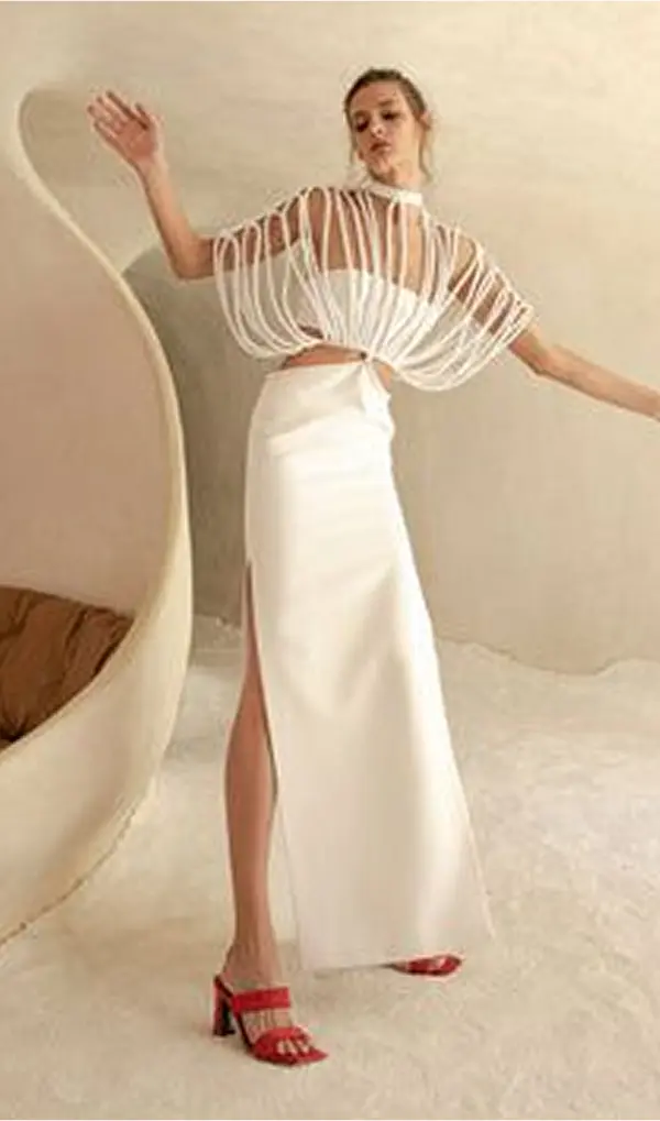 femme avec longue jupe blanche et court haut blanc, recouvert d'une deuxième top blanc, avec des fils espacés